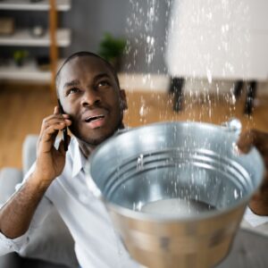 man on phone while holding bucket to capture leak