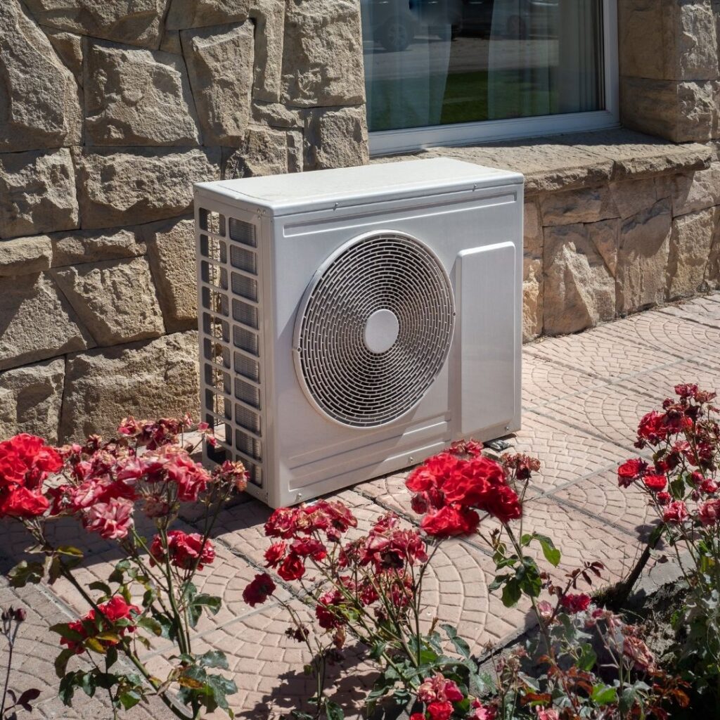 lone AC fan cabinet beside a flower bed
