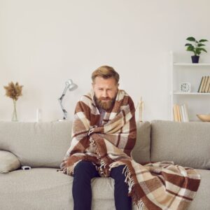 Person with an uncomfortable expression wrapped in a blanket while sitting on a couch