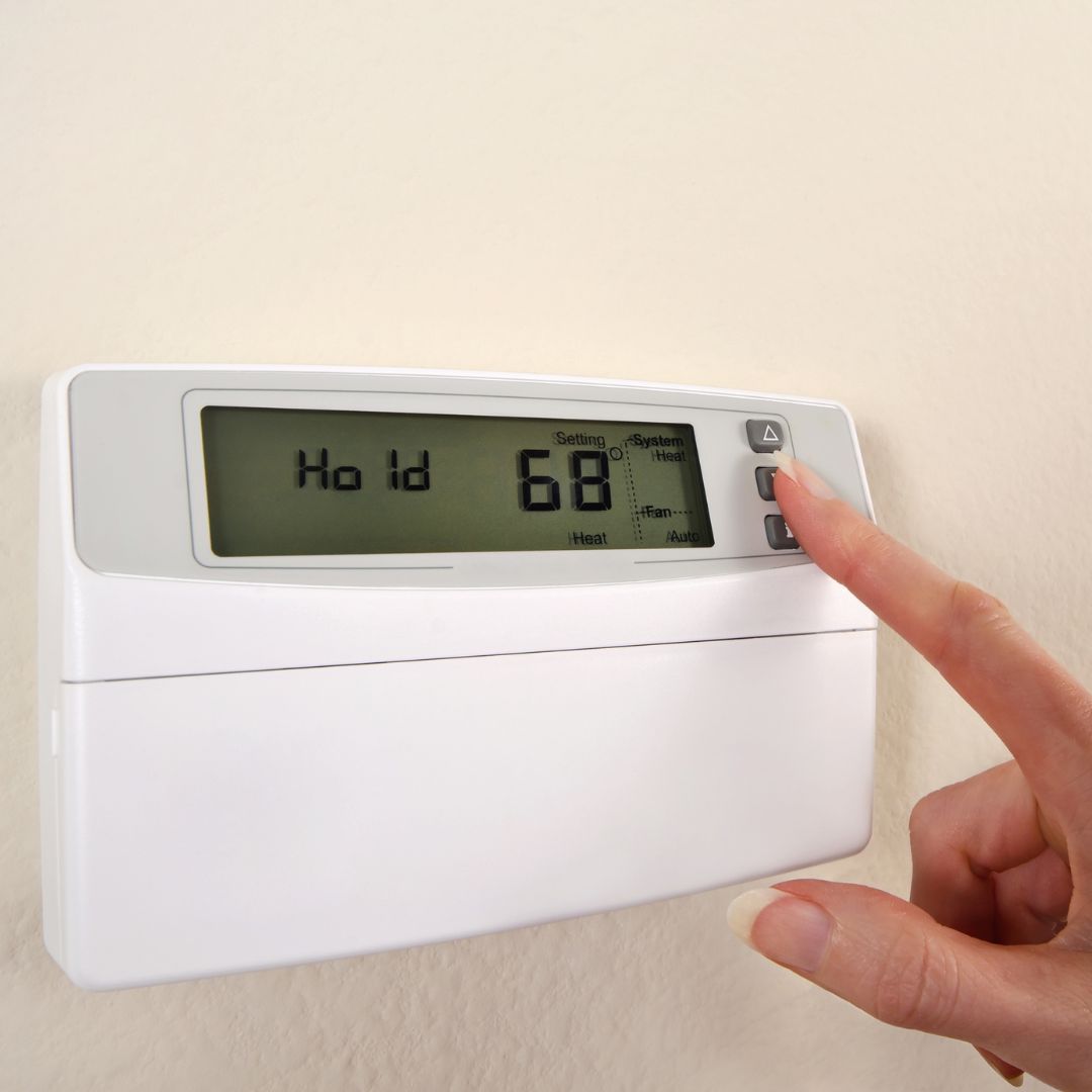 A close-up of a person's finger adjusting a thermostat.