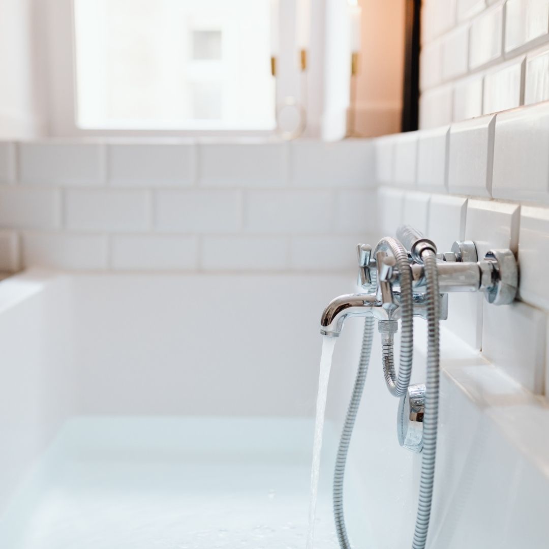 Chrome bathtub faucet running water in a bathroom with white subway tiles.
